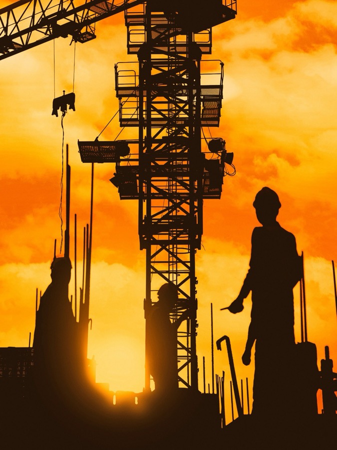 A construction crane and worker silhouetted against a dramatic sunset